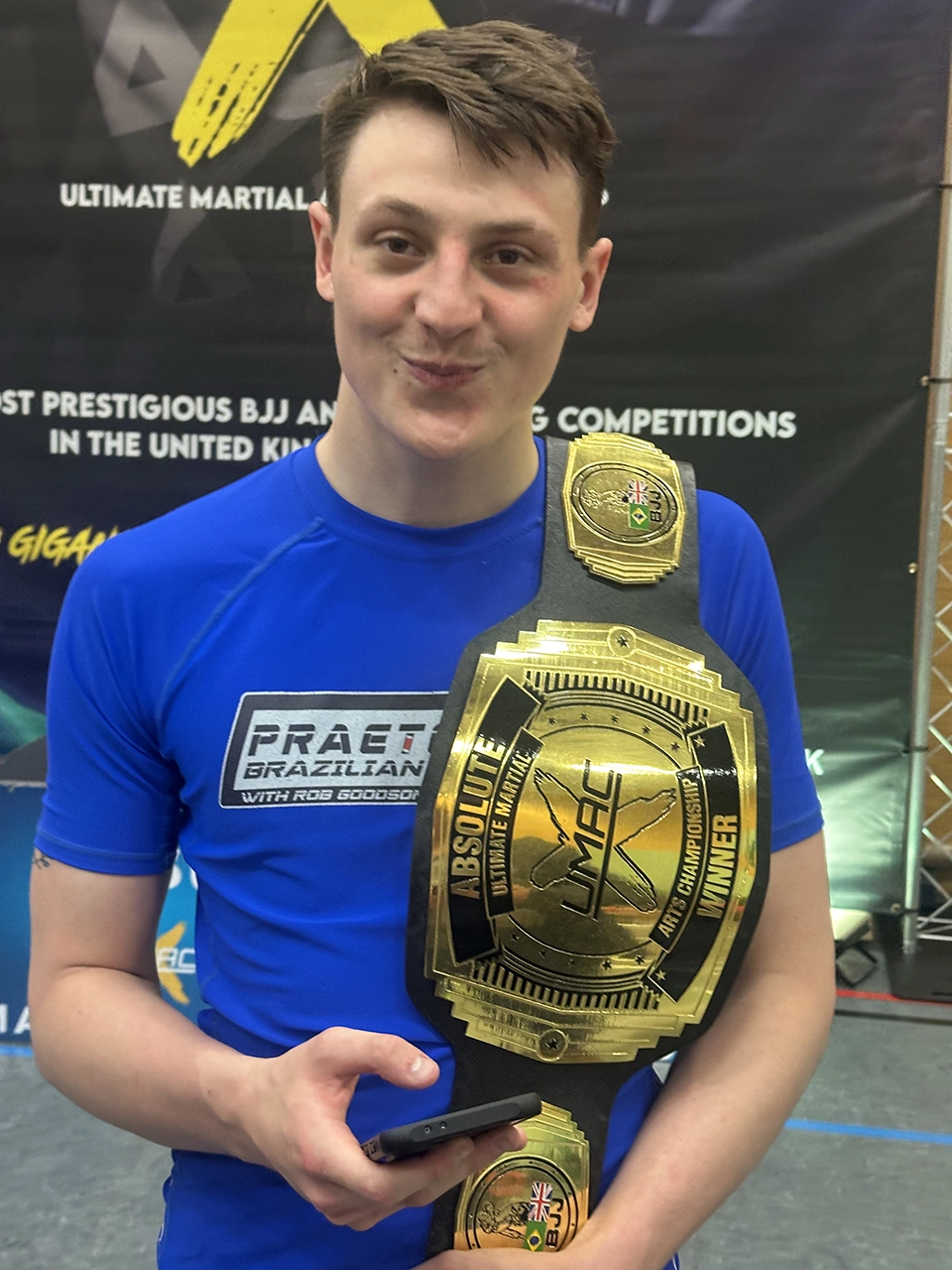Josh Woodbourne holding a Brazilian Jiu Jitsu championship belt after winning competition gold in 2026